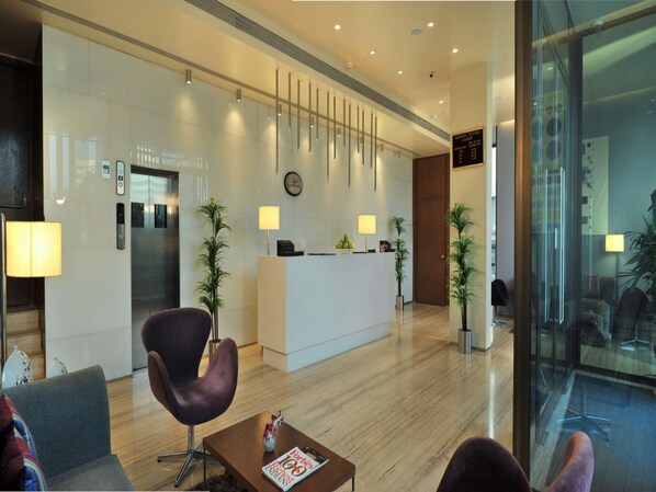 A modern hotel lobby with a reception desk, seating area, and elevator.