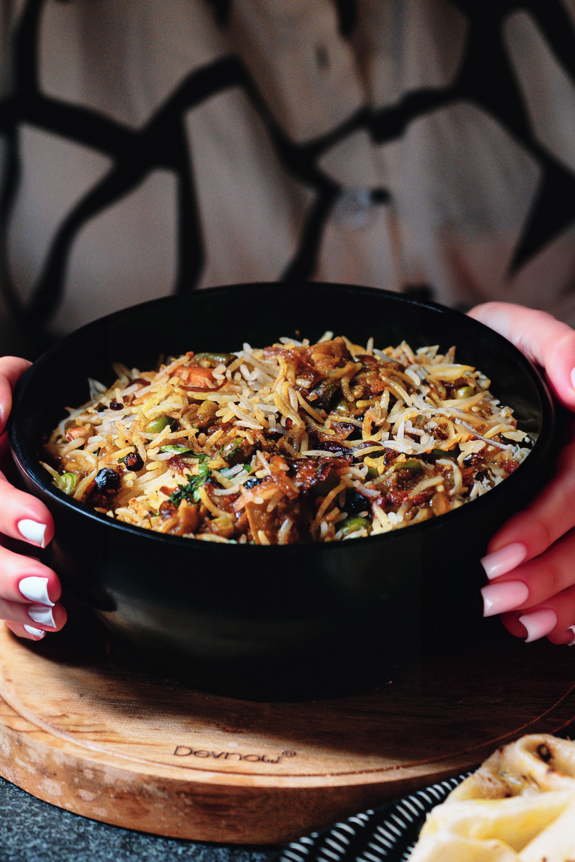 Un tazón de biryani sostenido por manos, con una tabla de madera debajo.