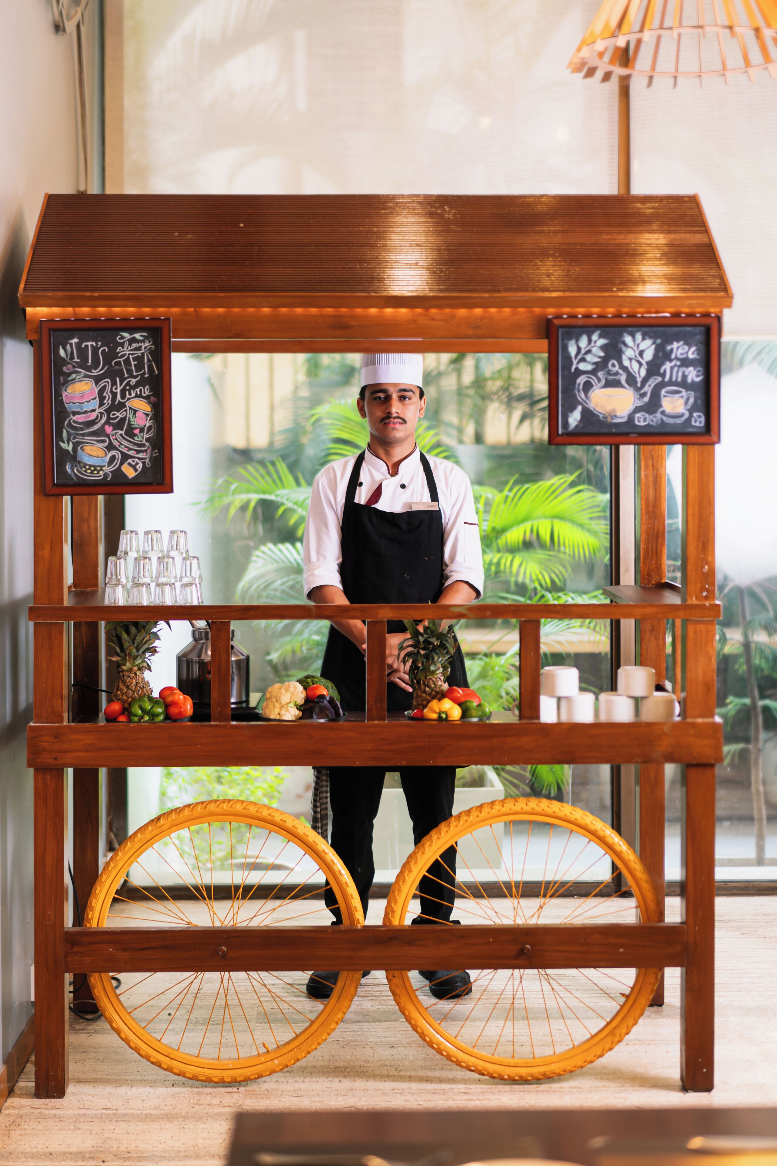 A wooden kiosk with a chef standing behind it, displaying fruits and beverages.