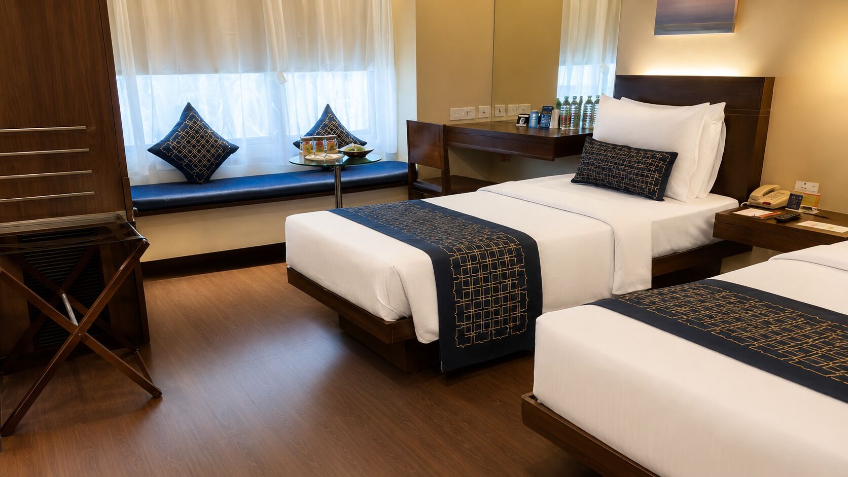 A hotel room with two beds, a desk, a chair, and a window with curtains.