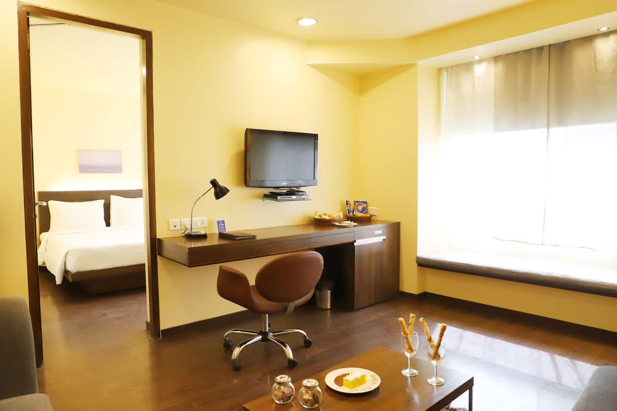 A hotel room with a bed, a desk with a computer, a television, and a window with curtains.