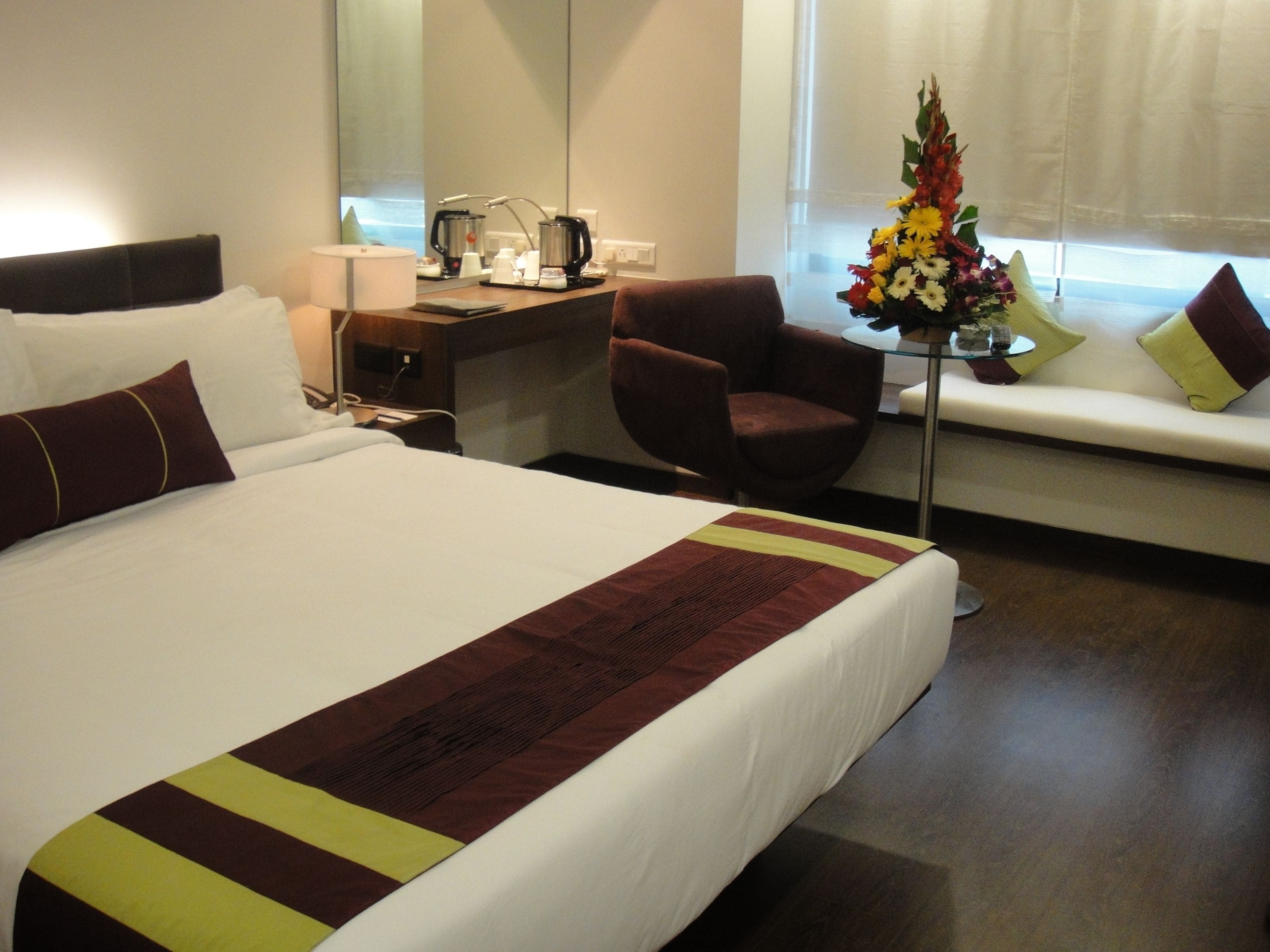 A hotel room with a large bed, a desk with a coffee maker, a chair, and a window with a view.