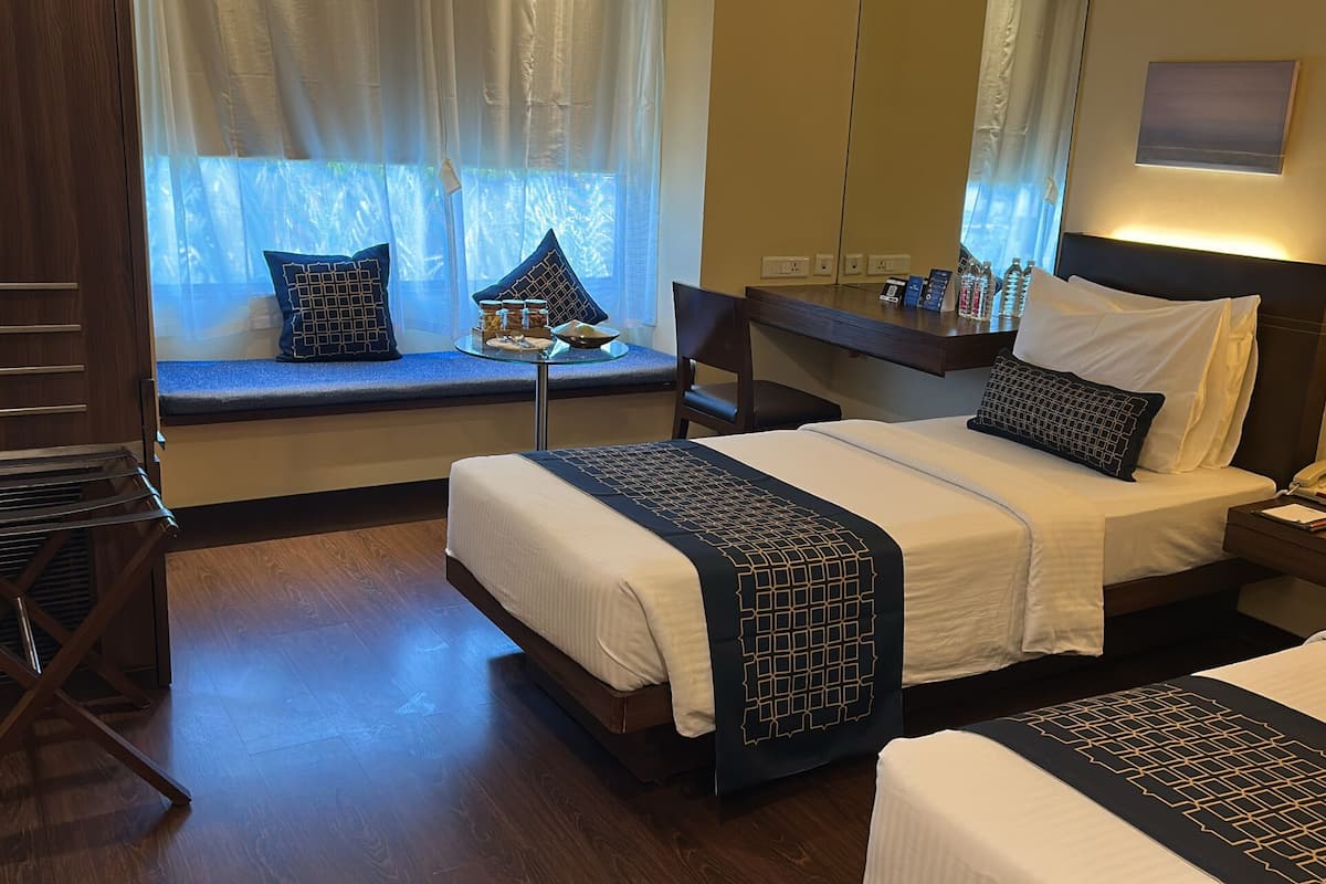 A hotel room with a bed, a chair, a small table, and a window with curtains.