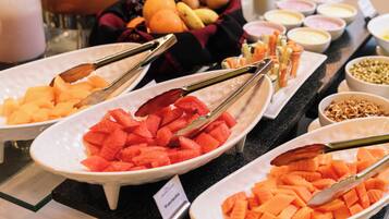 A buffet with various fruits and vegetables, including watermelon and carrots, arranged on white plates with tongs.