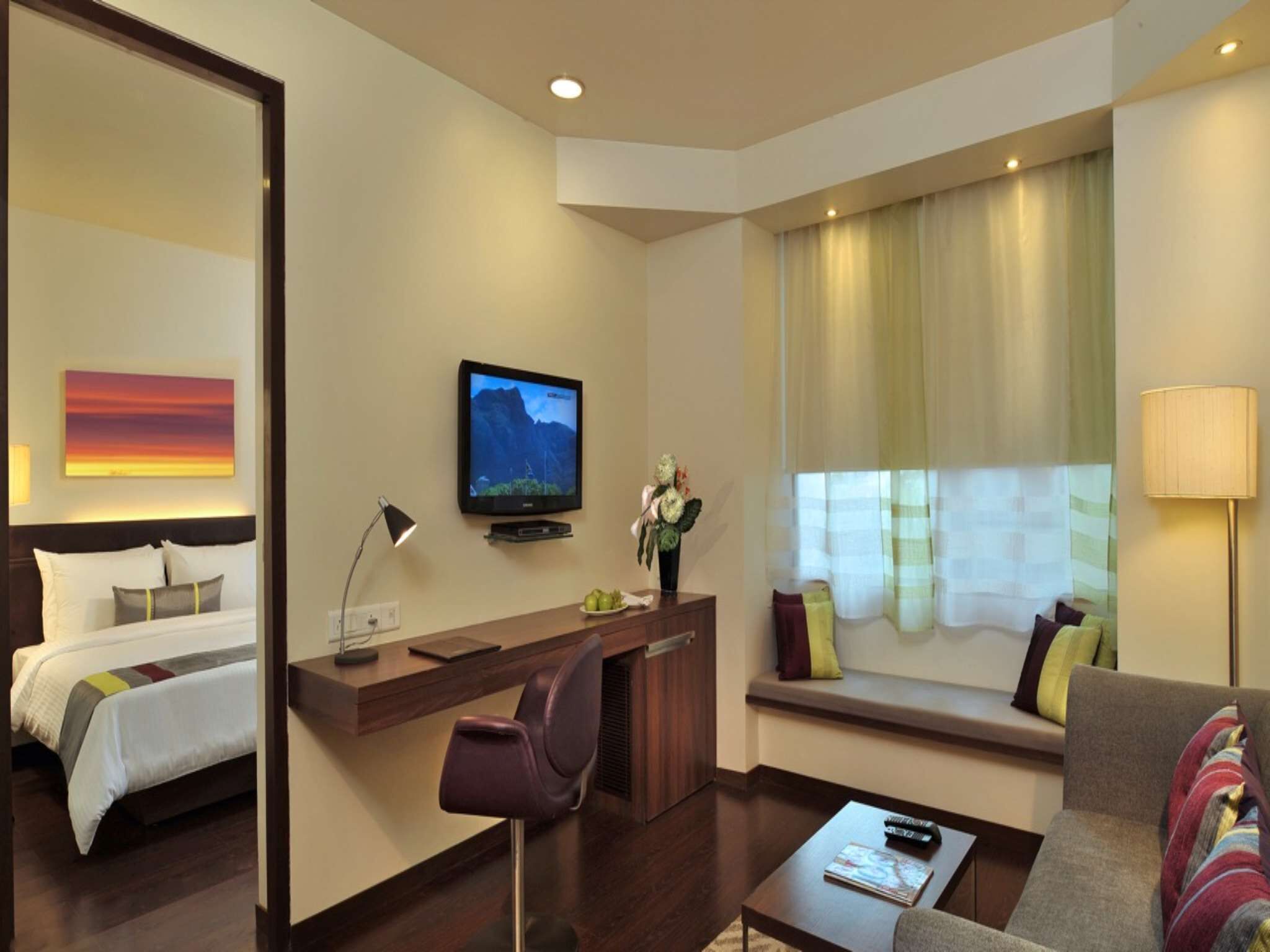 A hotel room with a bed, a desk with a chair, a television, a sofa, and a window with curtains.