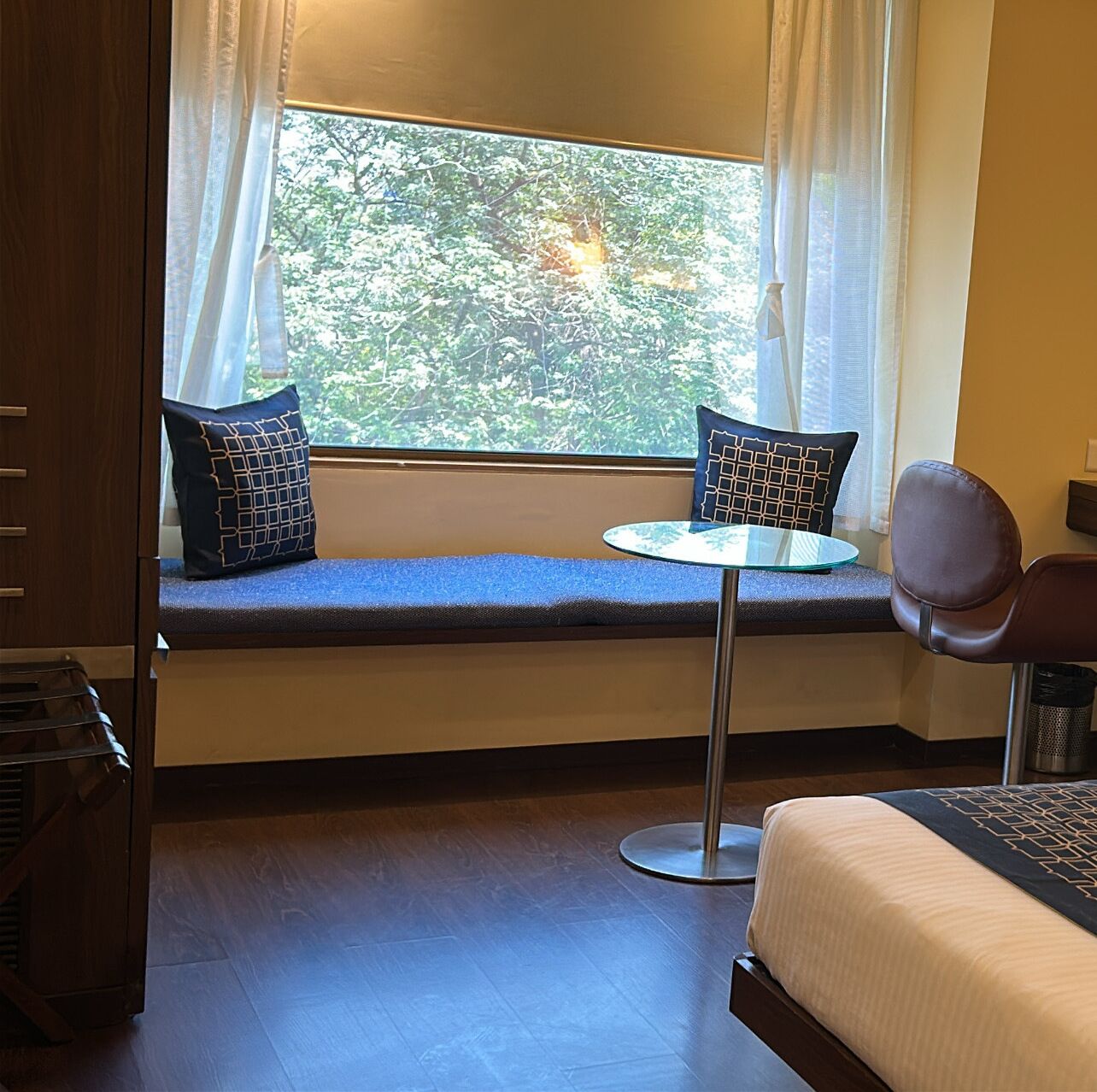 A room with a window seat, a small round table, a chair, and a bed.