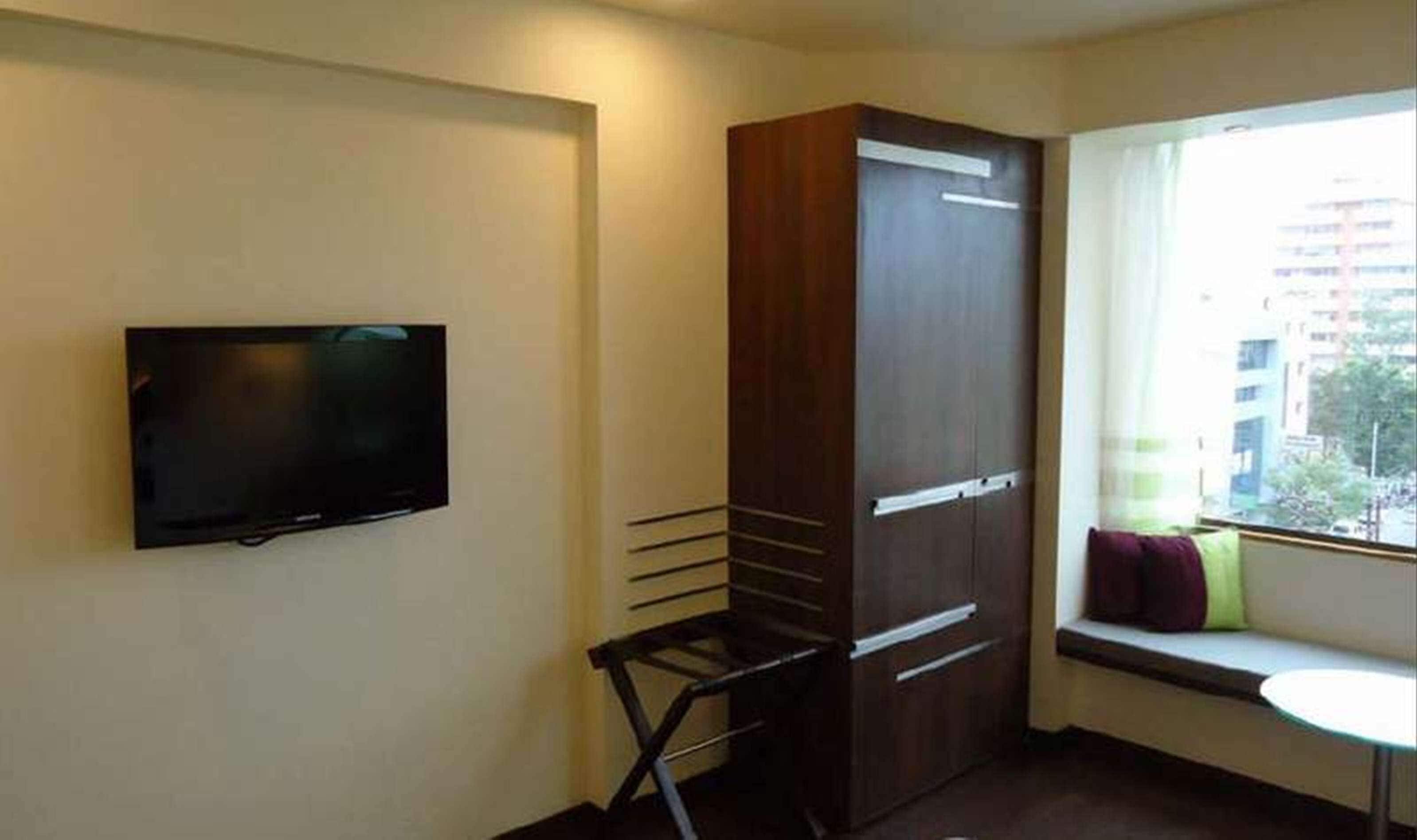 Habitació amb televisió penjada a la paret, un armari amb mirall i una finestra amb vista a edificis.