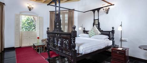A four-poster bed with a canopy, a bedside table, a nightstand, a small table with a vase, and a red carpet.