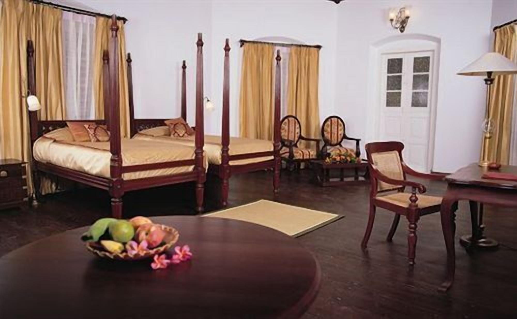 A four-poster bed with a wooden frame, a dining table with a fruit bowl, and two chairs.