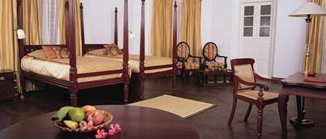 A four-poster bed with a wooden frame, a dining table with a fruit bowl, and two chairs.