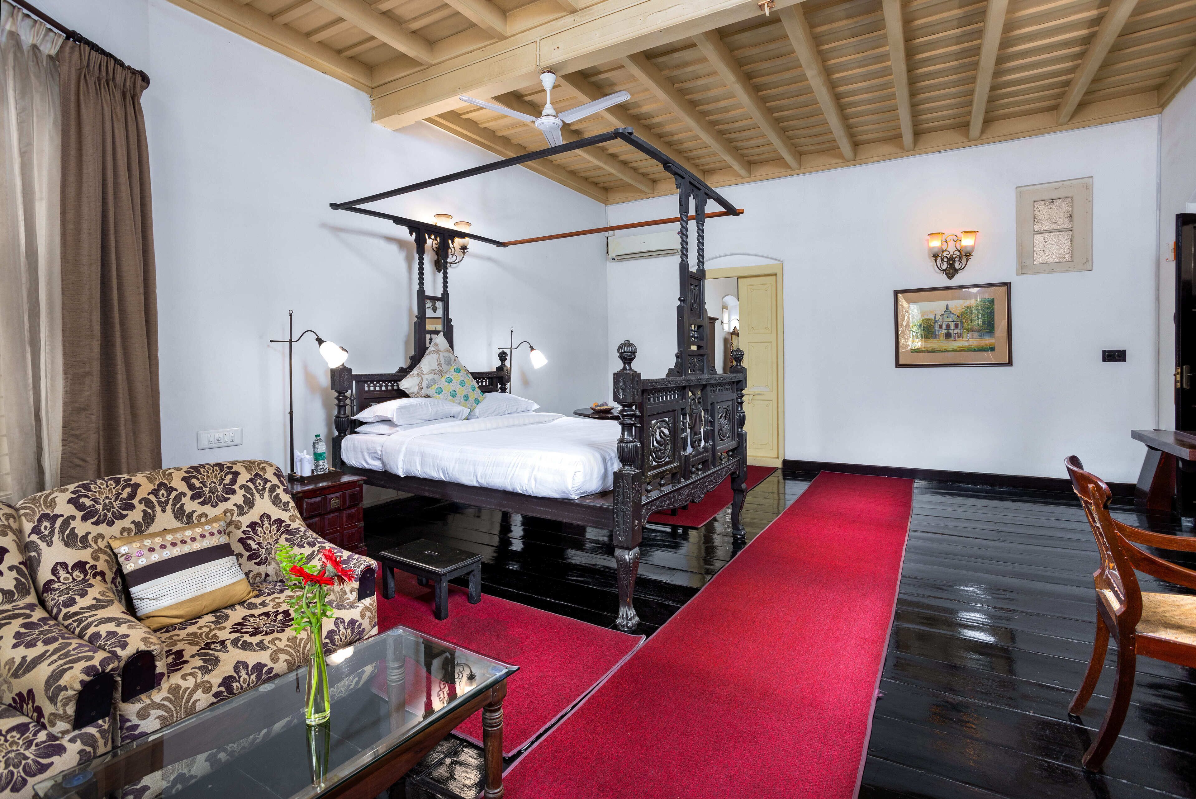 A bedroom with a four-poster bed, a sofa, a glass coffee table, and a red carpet.