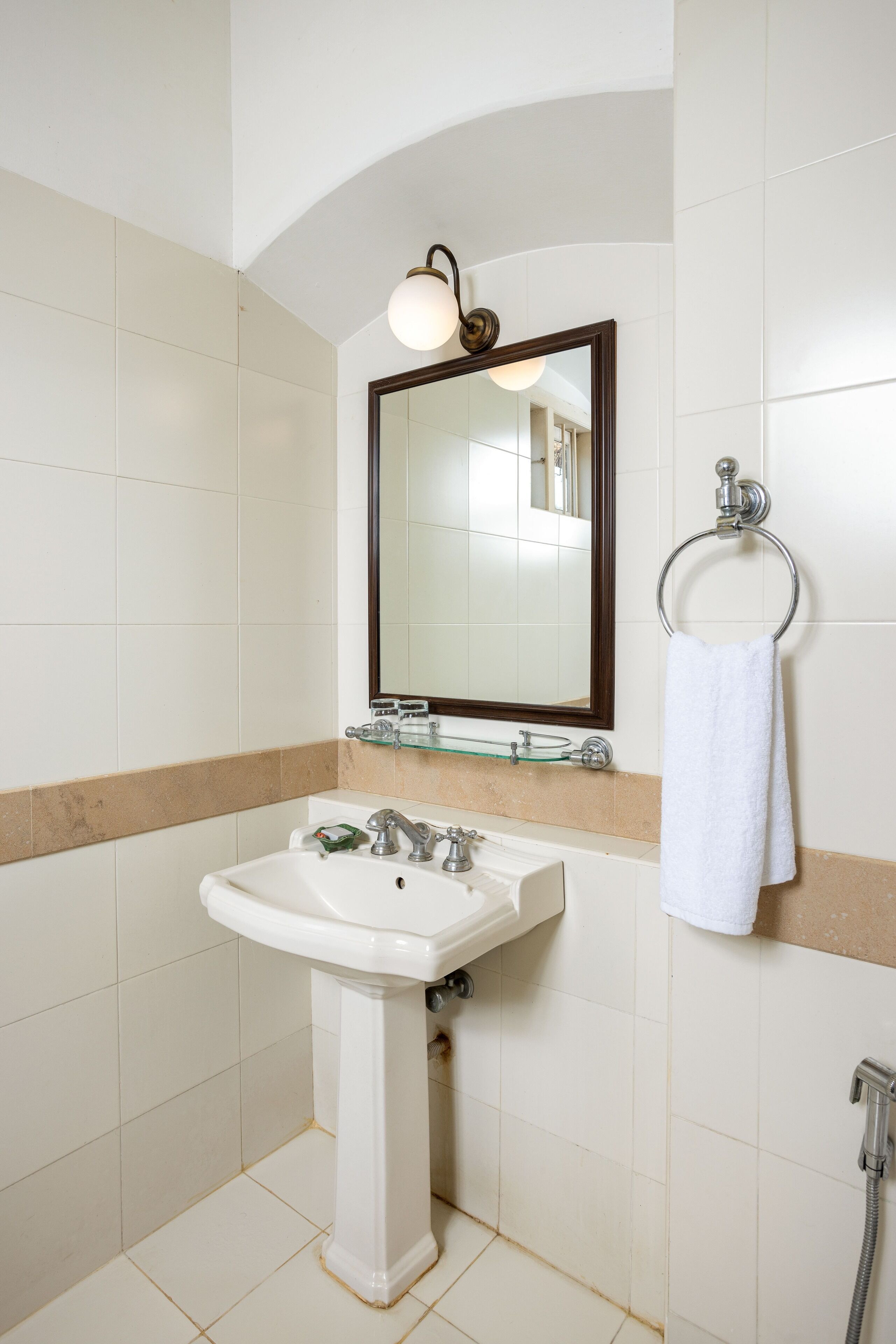 A bathroom with a pedestal sink, a mirror, a towel ring, and a shower.