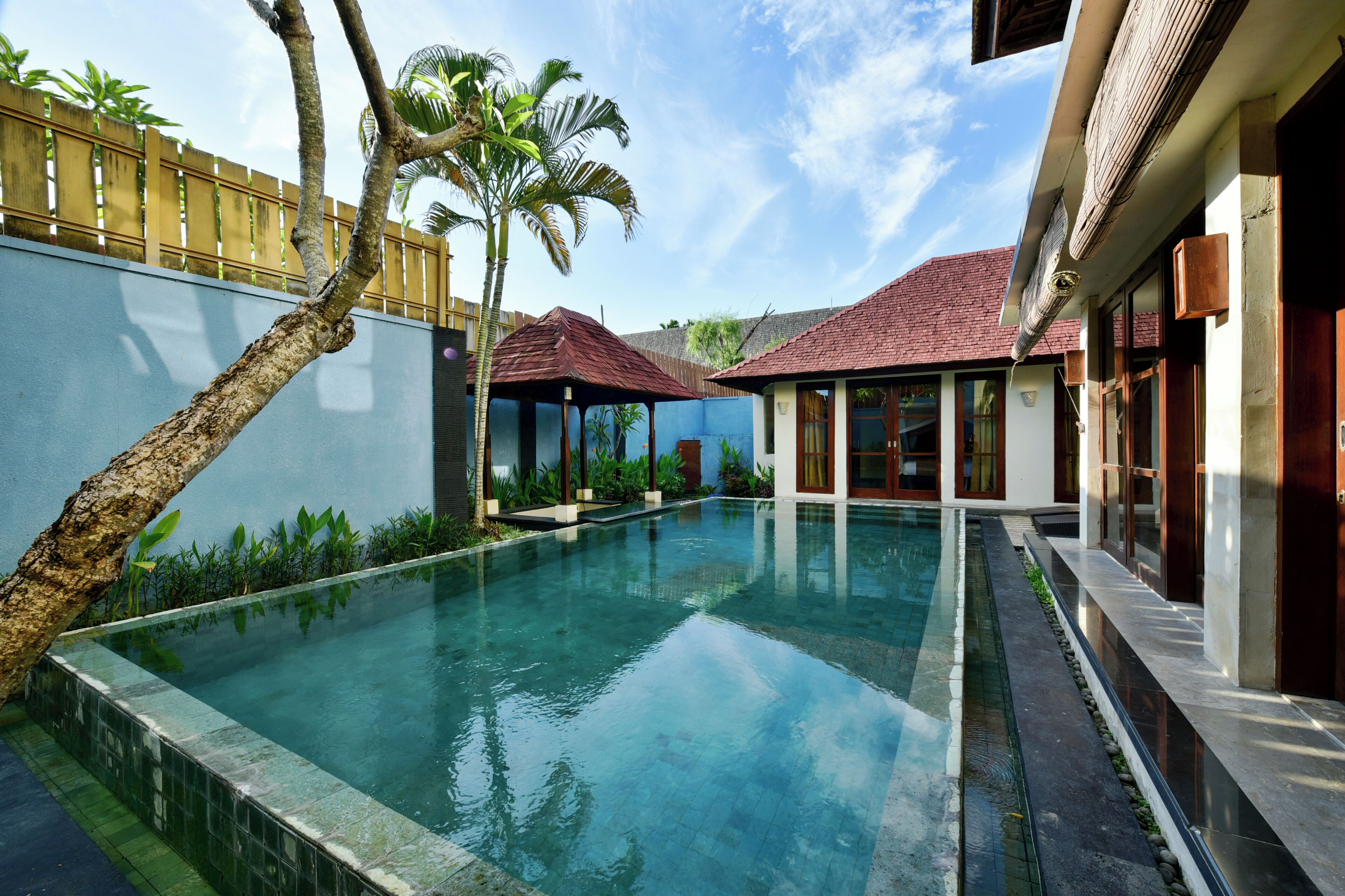A swimming pool with a clear blue water surface, surrounded by a low wall and a wooden fence.