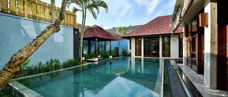 A swimming pool with a clear blue water surface, surrounded by a low wall and a wooden fence.
