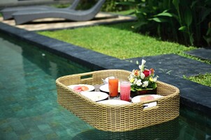 A wicker tray with plates, glasses, and a floral arrangement by a pool.