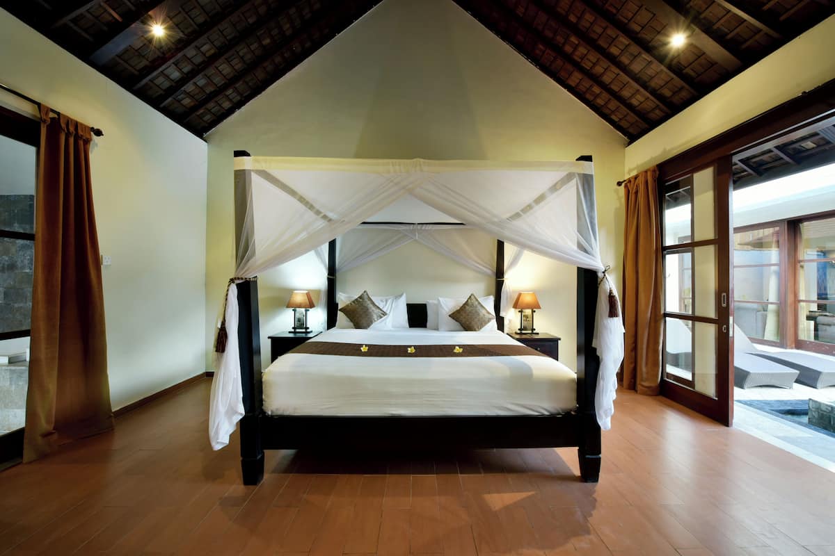 A large bed with a canopy, wooden floors, and two bedside lamps.
