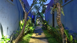 A narrow pathway flanked by blue walls and lush greenery, leading to a building with a checkered awning. - The Khayangan Dreams Villa Umalas (Kerobokan)