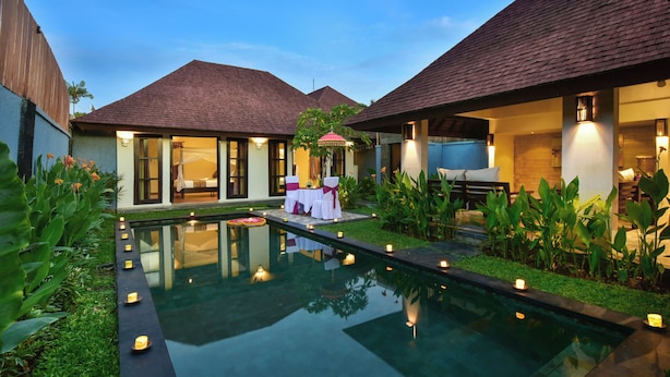 A pool area with a table set for two, surrounded by greenery and candles. - The Khayangan Dreams Villa Umalas (Kerobokan)
