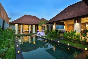 A pool area with a table set for two, surrounded by greenery and candles. - The Khayangan Dreams Villa Umalas (Kerobokan)