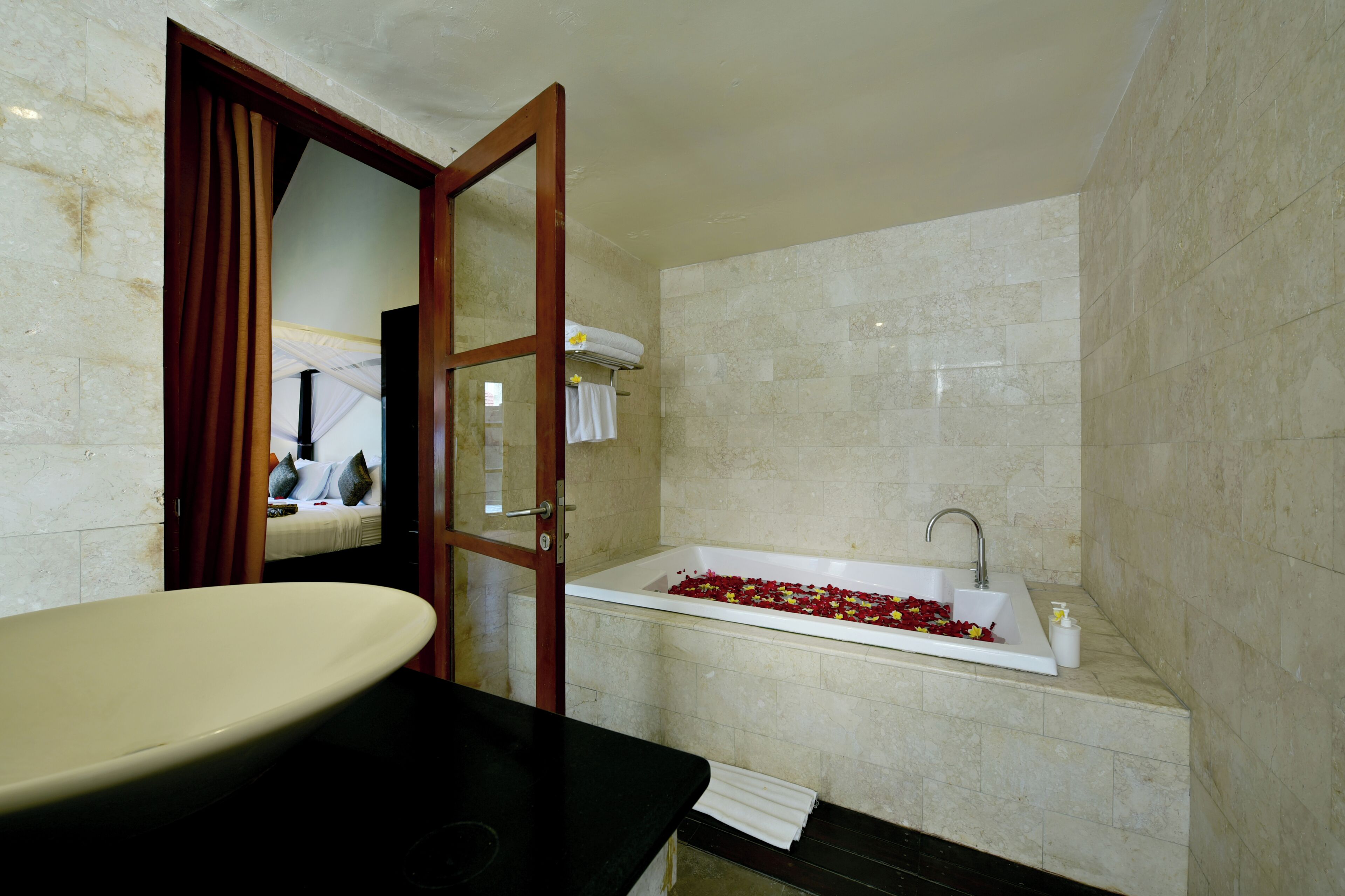 A bathroom with a bathtub filled with rose petals, a large sink, and a mirror.
