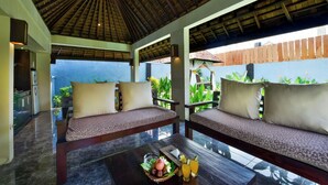 A room with a thatched roof, two sofas with cushions, a table with a fruit basket and drinks, and a view of the sea. - The Khayangan Dreams Villa Umalas (Kerobokan)
