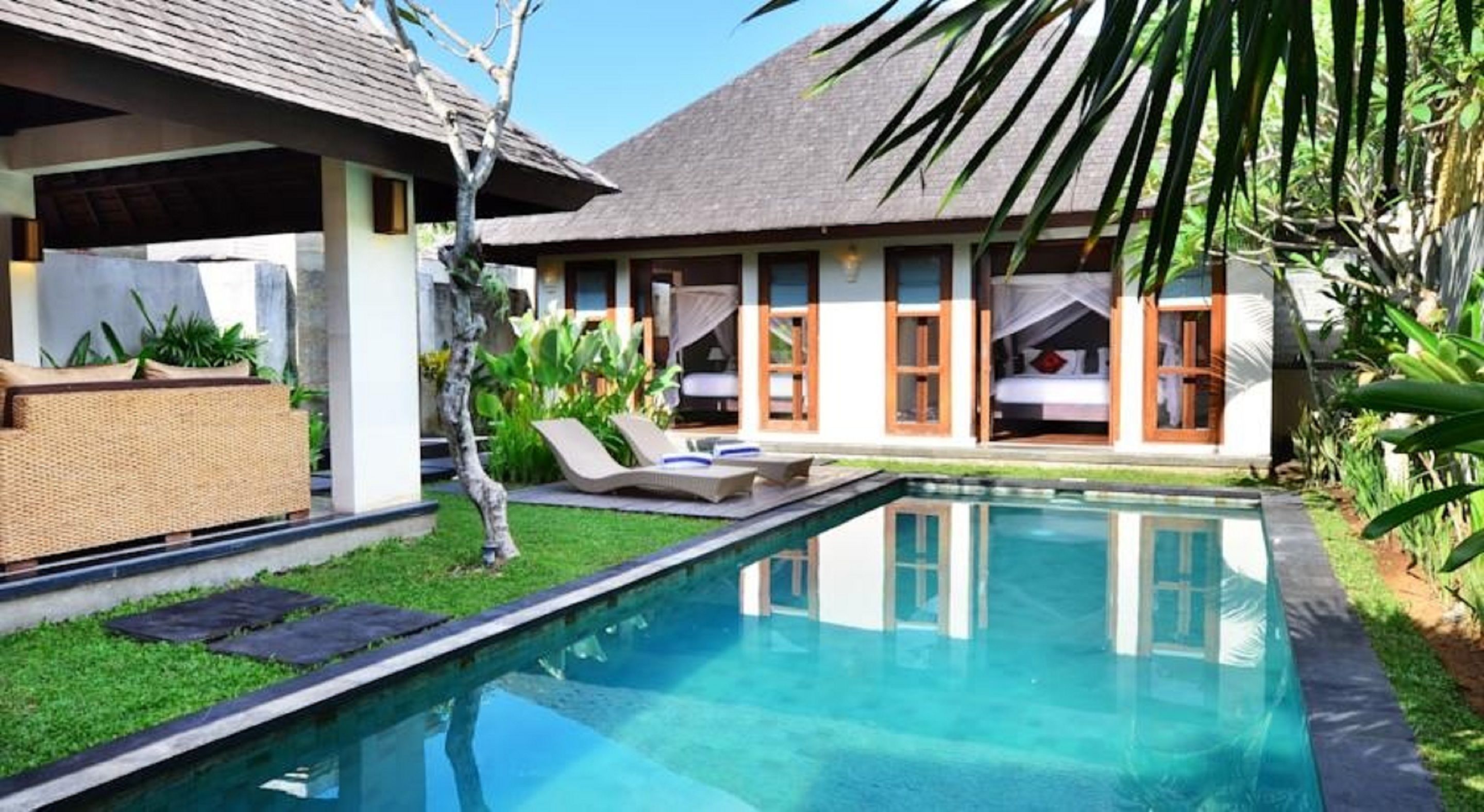 A poolside view of a resort with a clear pool, lounge chairs, and a building with multiple rooms.