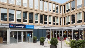 Un hôtel Travelodge doté d’une façade moderne, de grandes fenêtres et d’un espace extérieur aménagé avec des sièges.
