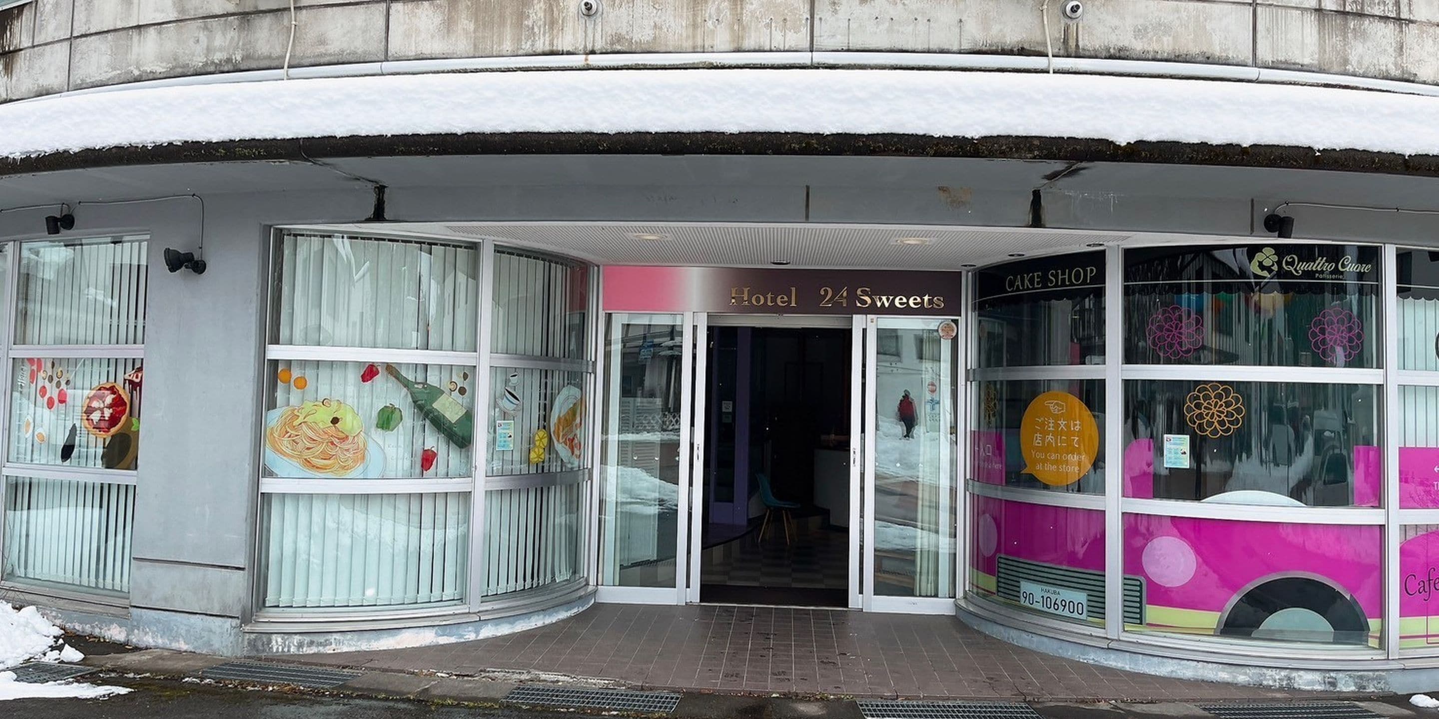 A hotel entrance with a glass door, a sign for 'Hotel 24 Sweets', and a cake shop with a pink sign.