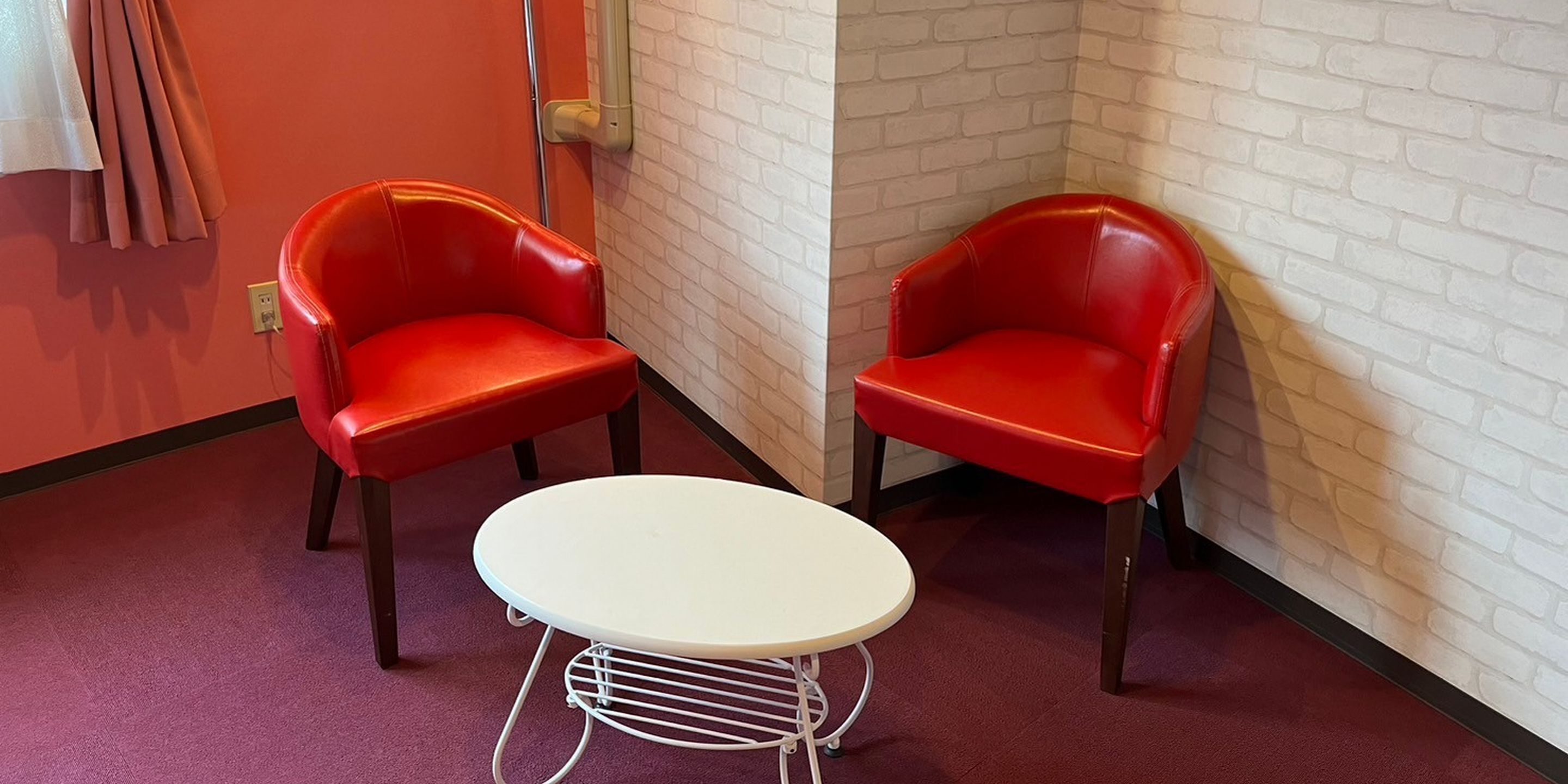 A corner with two red chairs and a small white table against a brick wall.