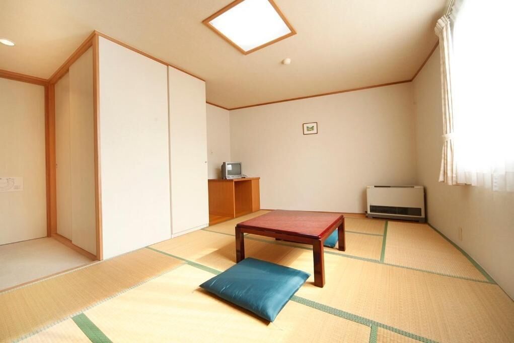 A room with tatami flooring, a low wooden table with a cushion, a wardrobe, a small cabinet, and a radiator.
