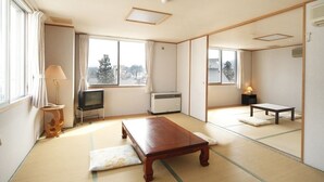 Una habitación tradicional japonesa con suelo de tatami, televisor, calentador y una pequeña mesa.