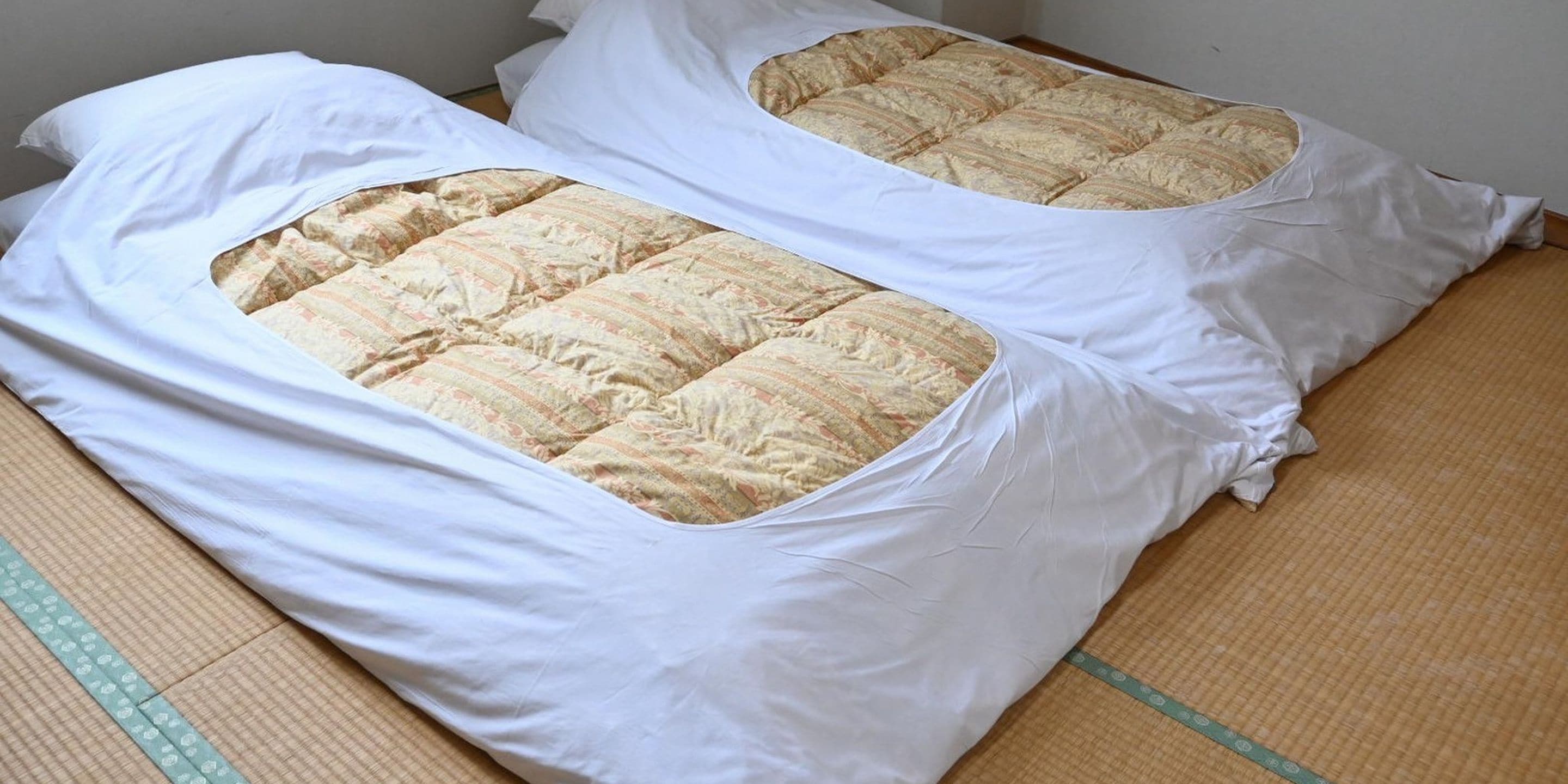 A room with two tatami mat beds covered with white bedding.