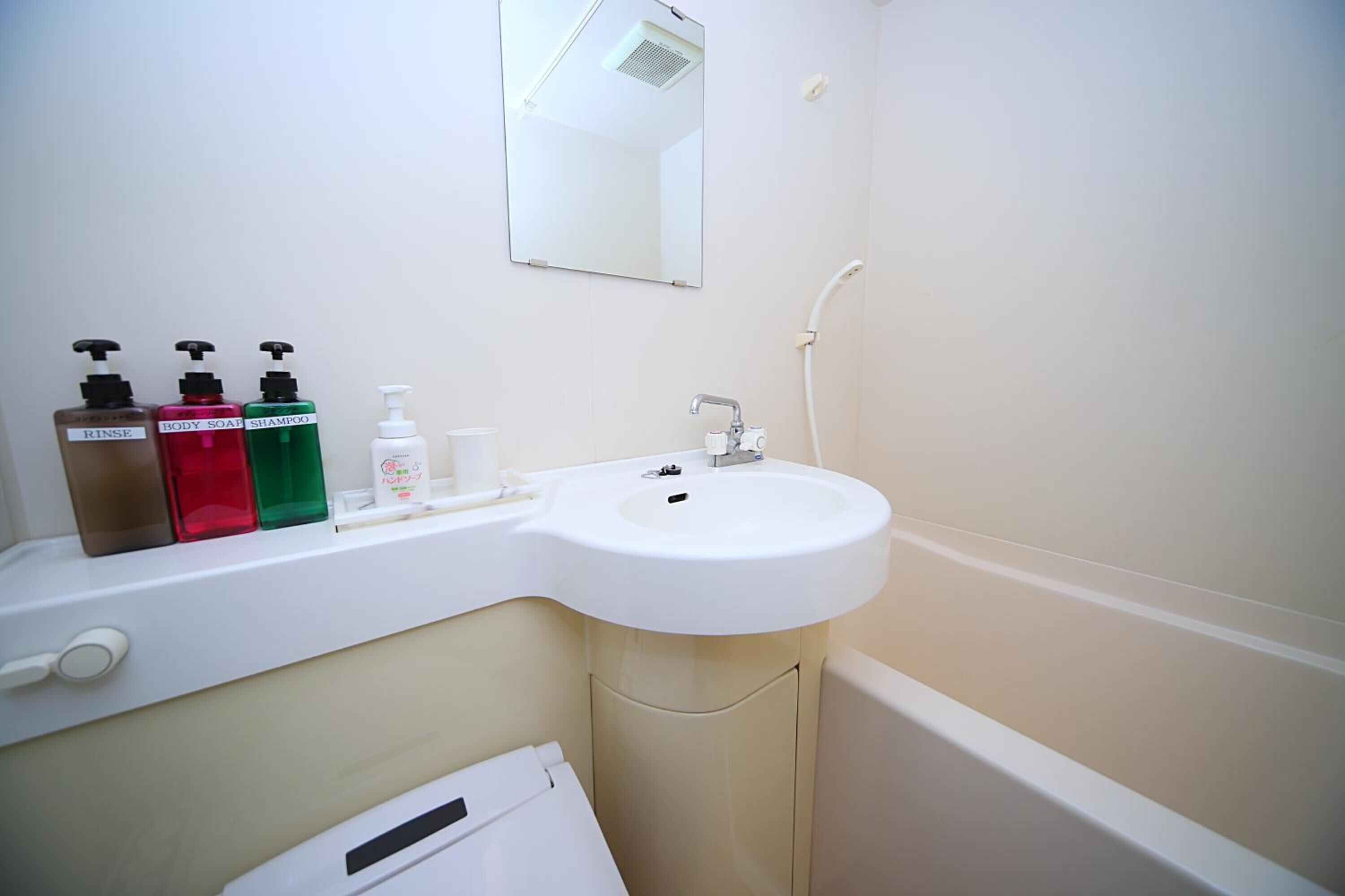 A bathroom with a sink, mirror, and three soap dispensers.