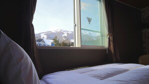 Habitación de hotel con cama, ventana con cortinas y vista a montañas nevadas.