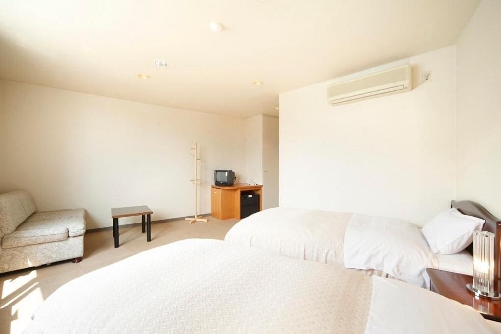 Een hotelkamer met een bed, een slaapbank, een klein tafeltje, een bureau met een computer en een televisie.