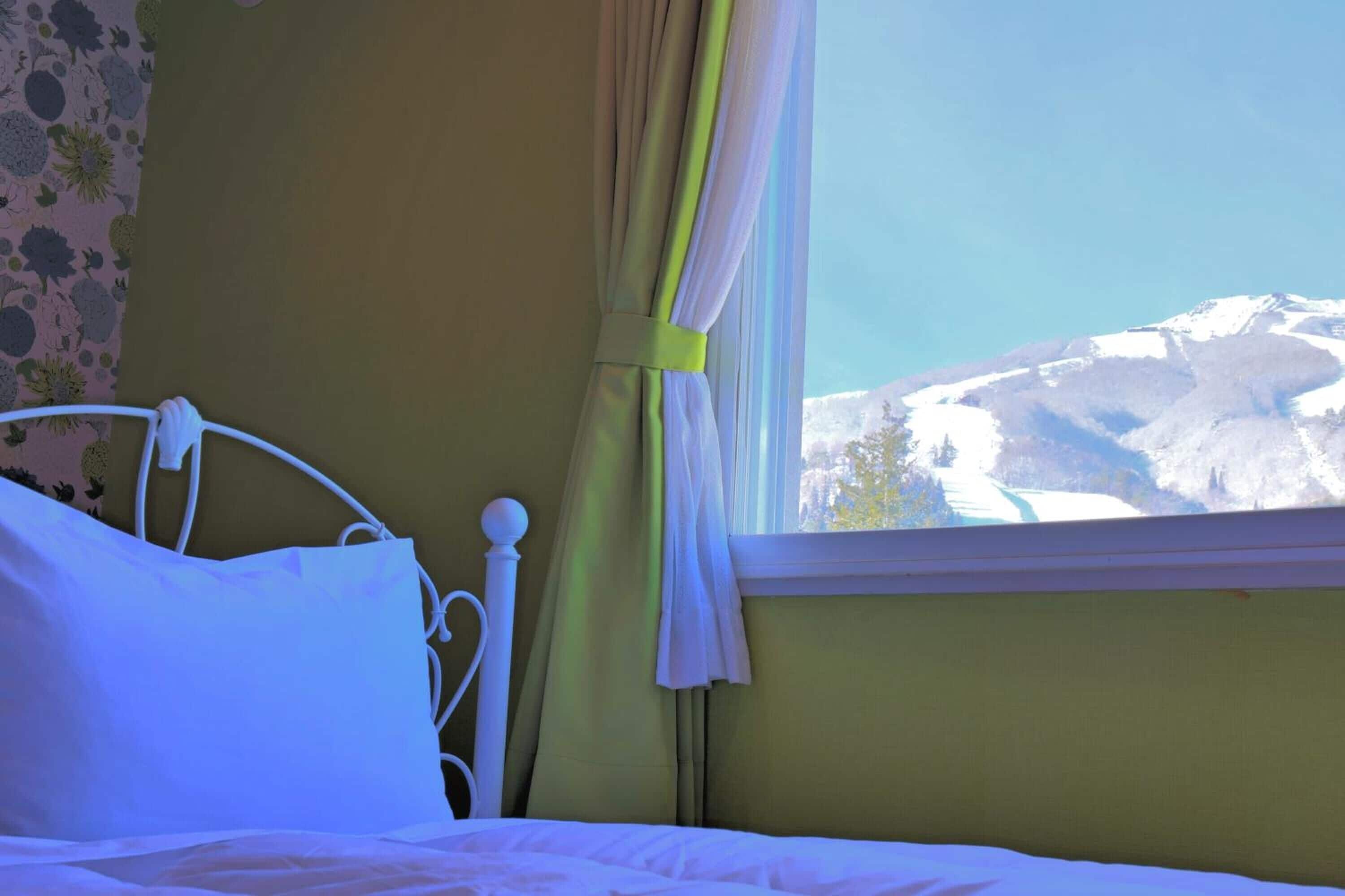 A bedroom with a bed, a window with curtains, and a view of a snowy mountain.