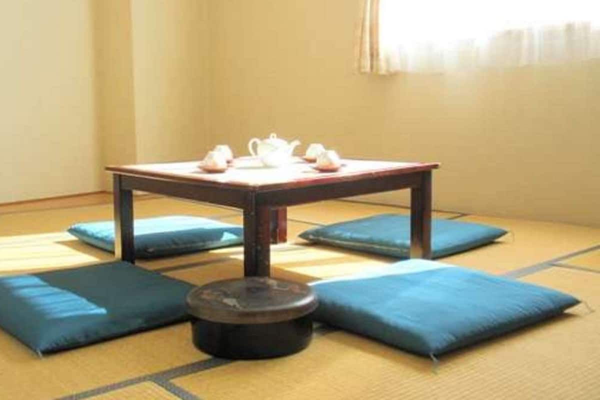 A tatami mat room with a low table, cushions, and a round container.
