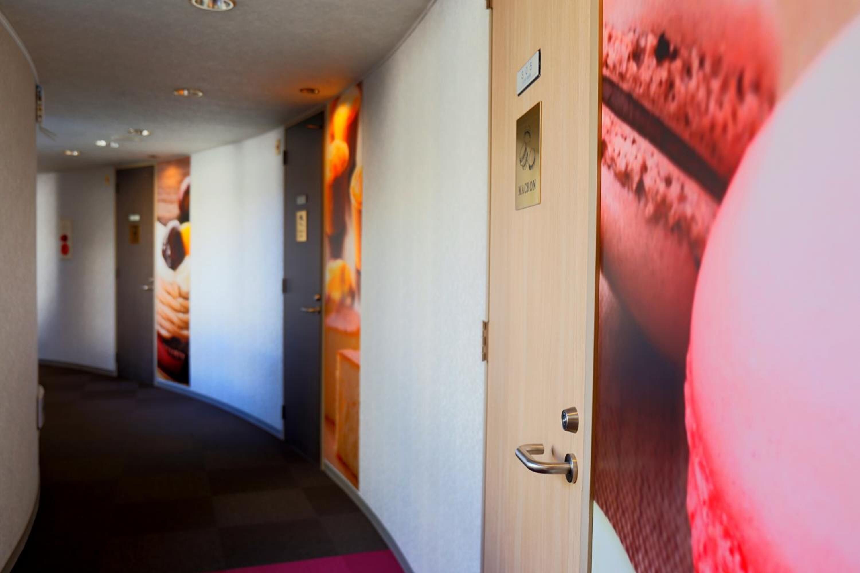 A hotel corridor with a wooden door, a wall-mounted sign, and a poster of a dessert.