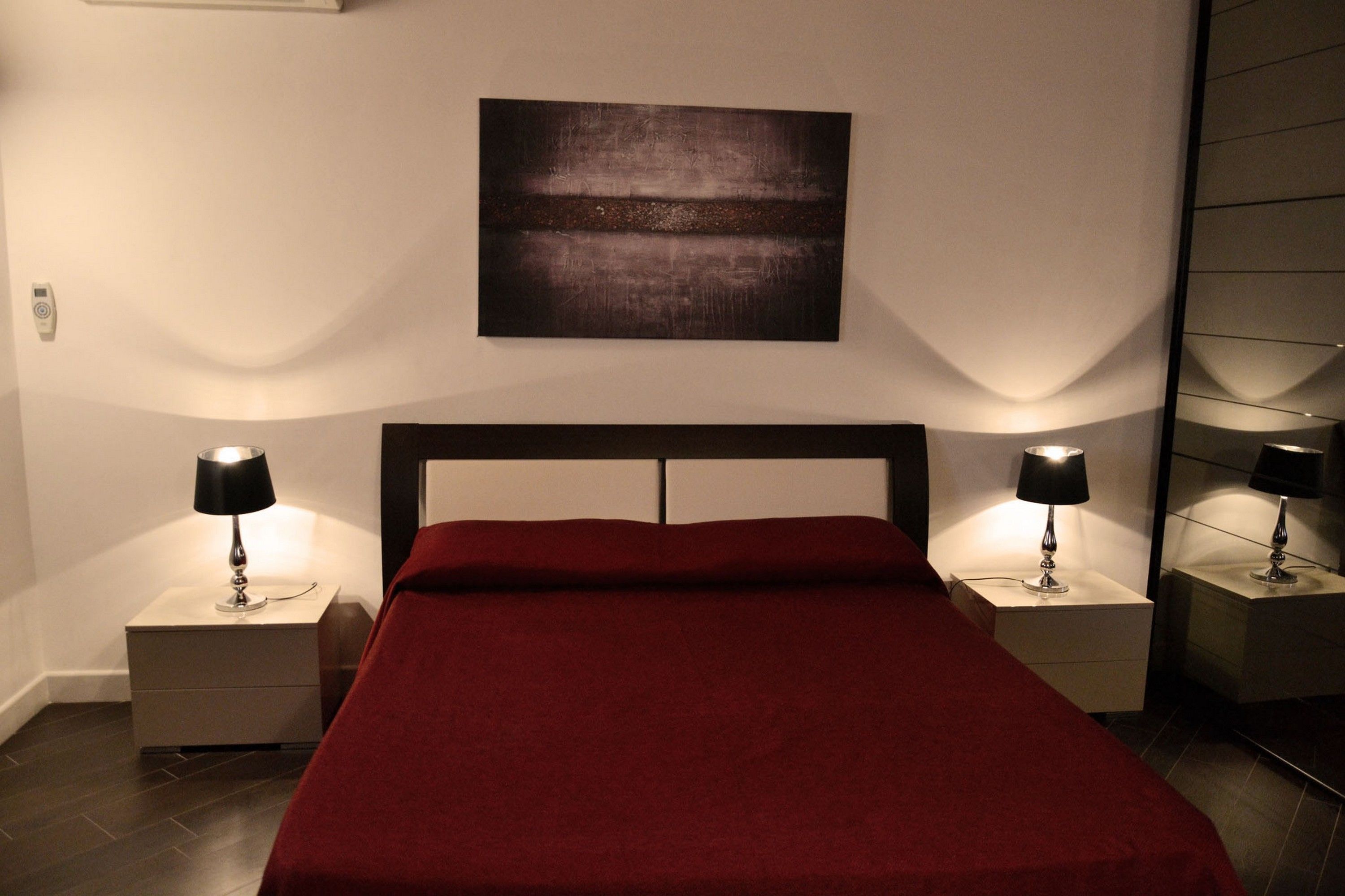 A bedroom with a large bed, two bedside tables with lamps, a wall-mounted artwork, and a modern design.