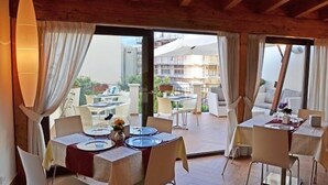 A dining area with tables set for two, large windows with curtains, and a view of a building with scaffolding.