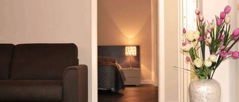 A living room with a dark brown sofa, a white vase with flowers, and a lamp in the background.