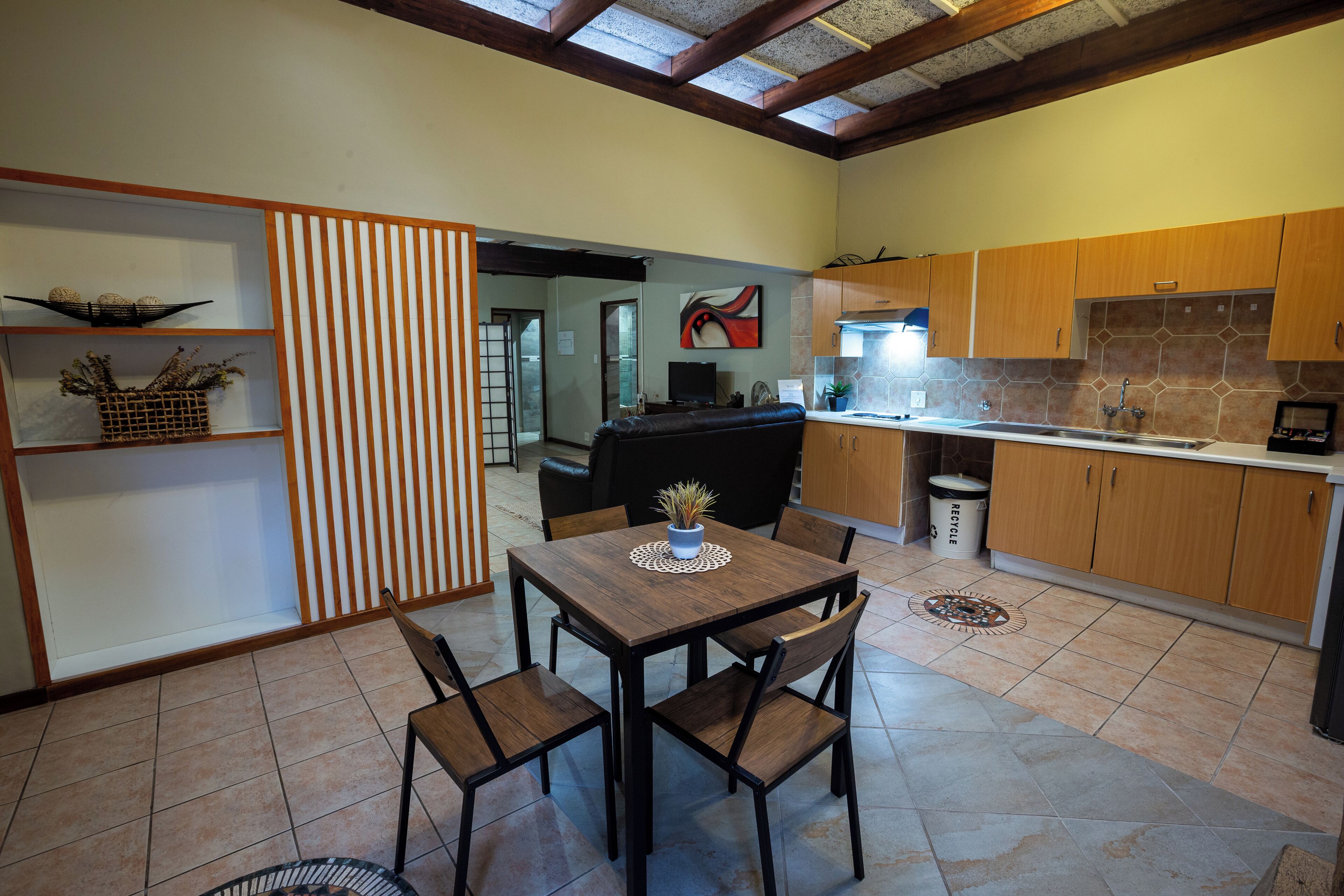 Une cuisine avec des meubles de rangement en bois, une table à manger avec quatre chaises et une petite plante en pot posée sur la table.