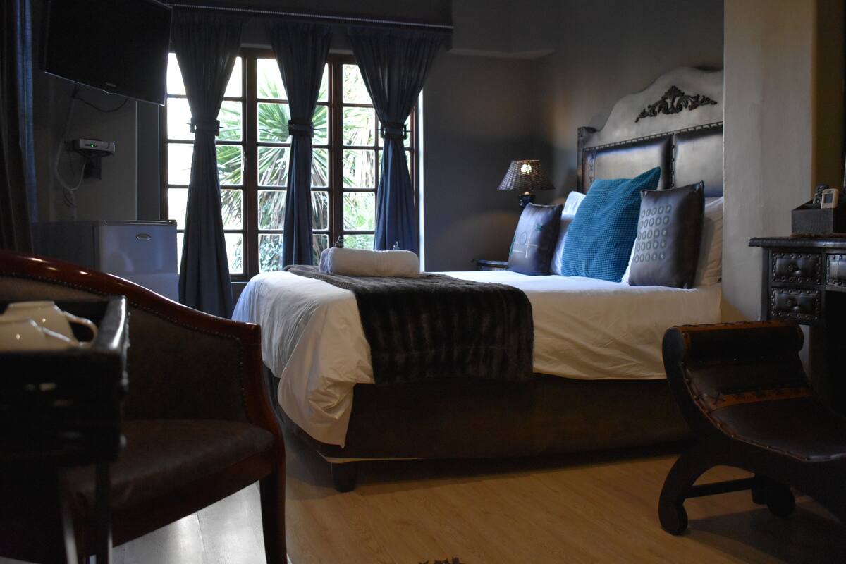 A bedroom with a large bed, a desk with a lamp, and a chair.