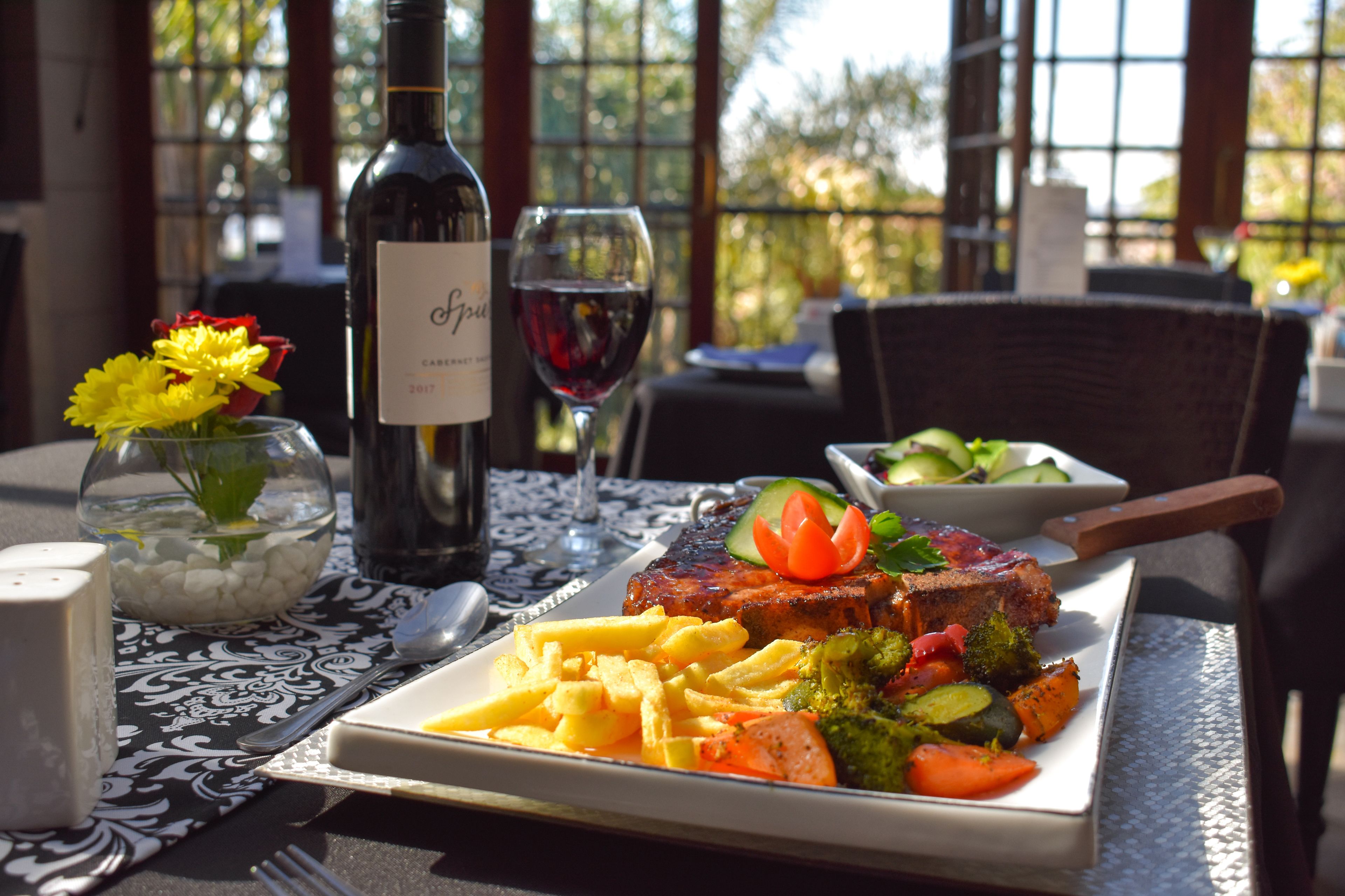 Una mesa de comedor con un plato de comida, una botella de vino y una copa de vino tinto.