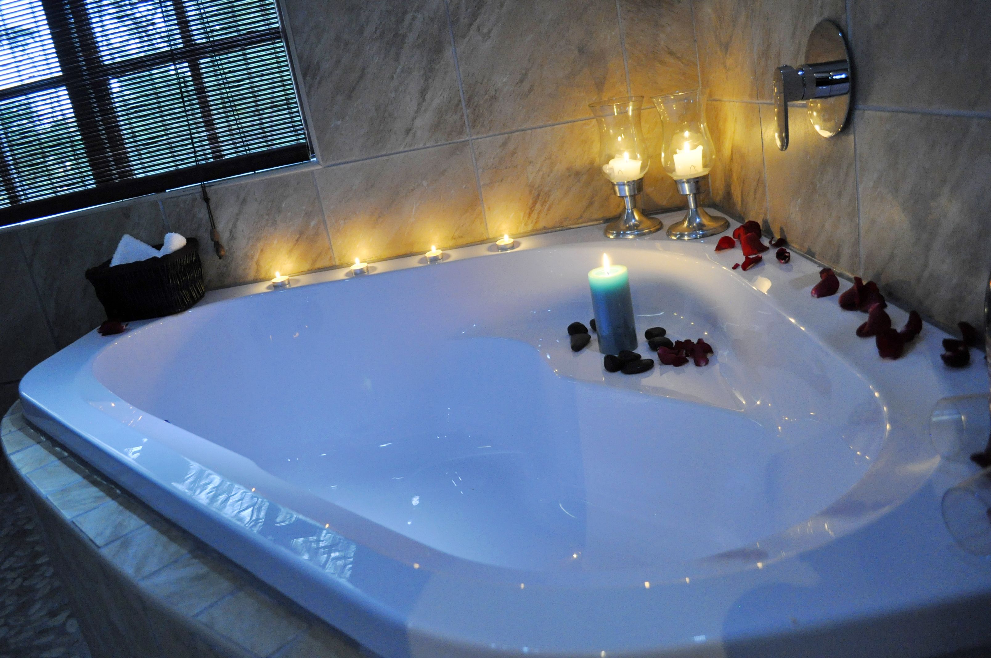 Eine große Badewanne mit Kerzen und Rosenblättern, ein Korb mit Handtüchern und ein Fenster mit Jalousien.