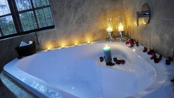 Eine große Badewanne mit Kerzen und Rosenblättern, ein Korb mit Handtüchern und ein Fenster mit Jalousien.