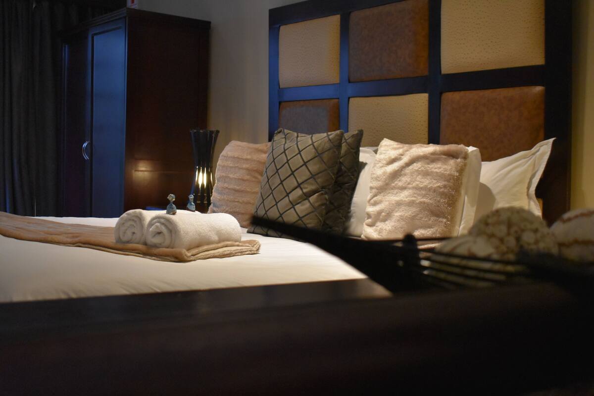 A neatly made bed with rolled towels, a tray with a fork and spoon, and a decorative vase.