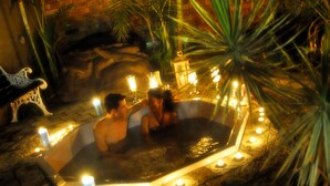 A hot tub surrounded by candles and palm plants, set against a brick wall. - Waterfalls Boutique Hotel (Pretoria)