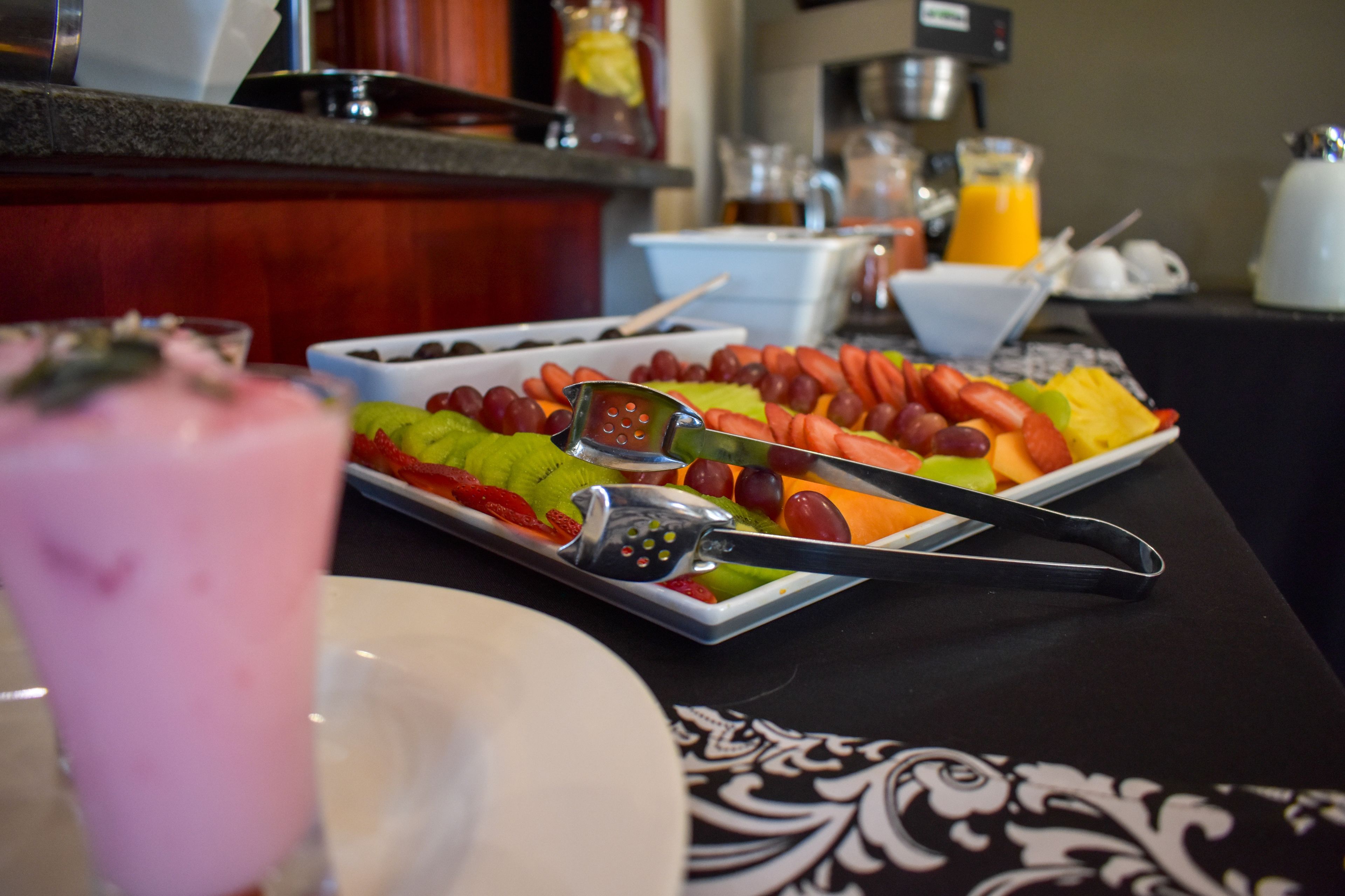 A breakfast buffet with various fruits and a pink beverage.