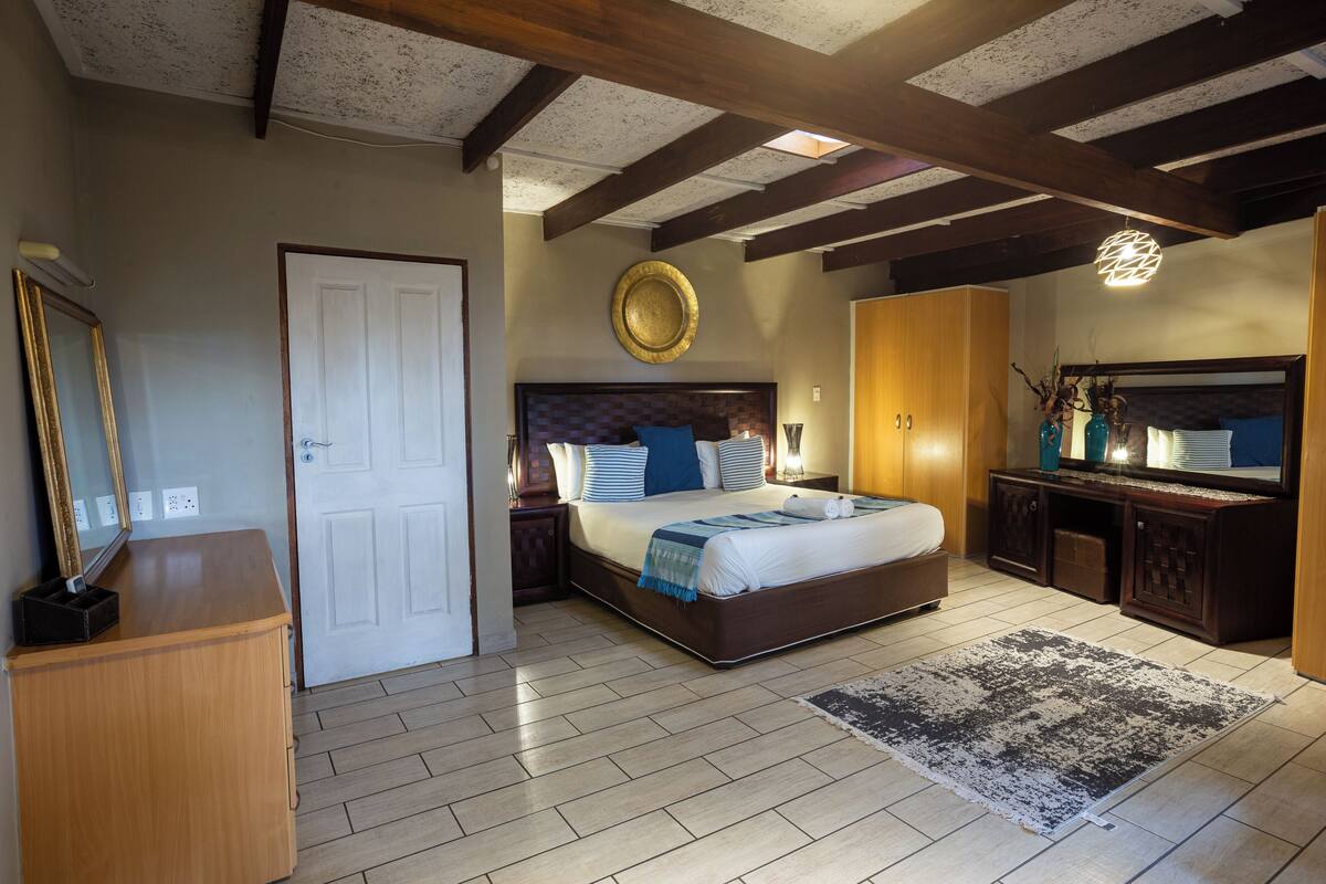A bedroom with a large bed, wooden headboard, a bedside table, a dresser, and a mirror.